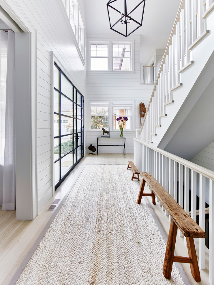 This is an example of an expansive beach style foyer in New York with white walls, light hardwood floors, a double front door and a glass front door.