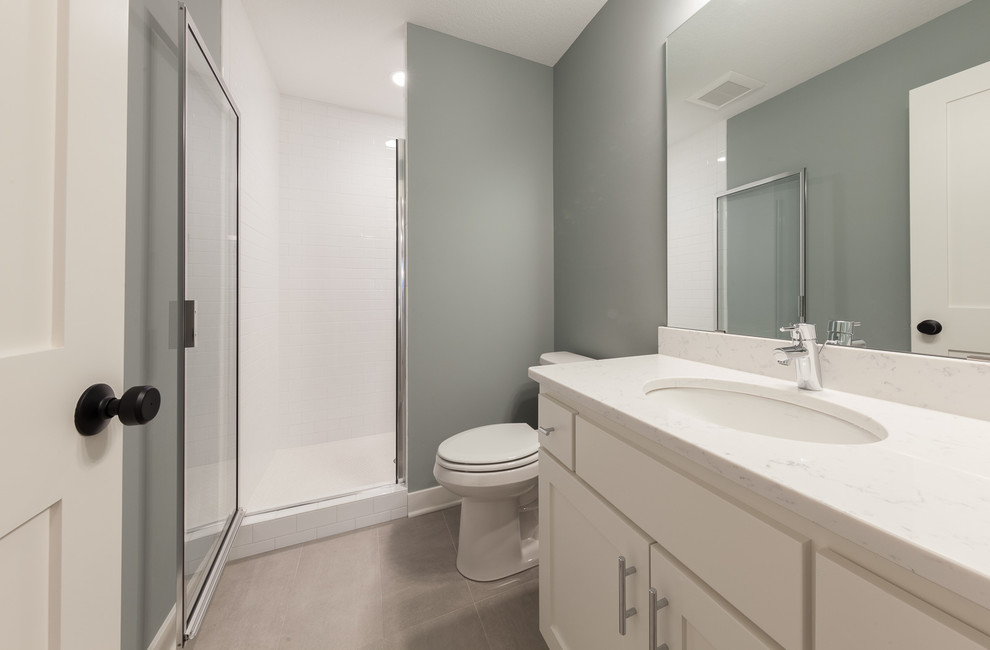 Mid-sized transitional 3/4 bathroom in Minneapolis with shaker cabinets, white cabinets, a two-piece toilet, white tile, subway tile, an undermount sink, marble benchtops, a hinged shower door, an alcove shower, grey walls, ceramic floors and grey floor.