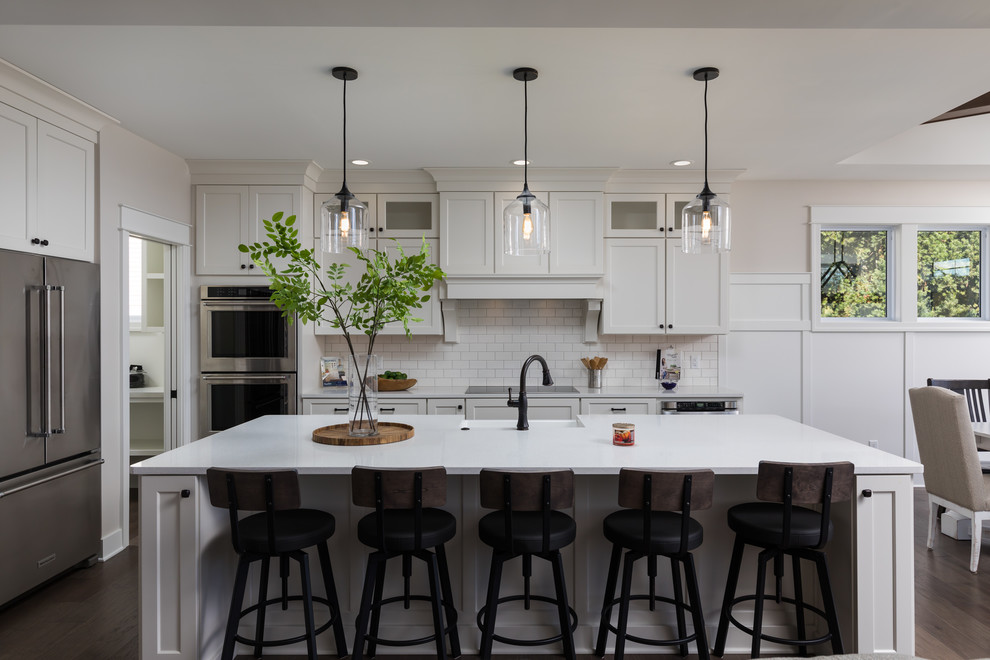 Inspiration for a mid-sized beach style galley eat-in kitchen in Grand Rapids with a farmhouse sink, white cabinets, quartzite benchtops, white splashback, subway tile splashback, stainless steel appliances, with island, brown floor, white benchtop, shaker cabinets and dark hardwood floors.