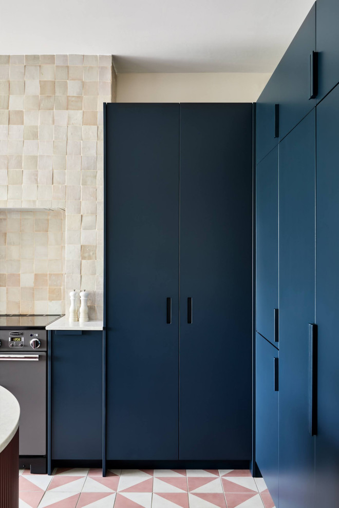 Large contemporary l-shaped eat-in kitchen in London with flat-panel cabinets, blue cabinets, solid surface benchtops, beige splashback, ceramic splashback, concrete floors, with island, pink floor and grey benchtop.
