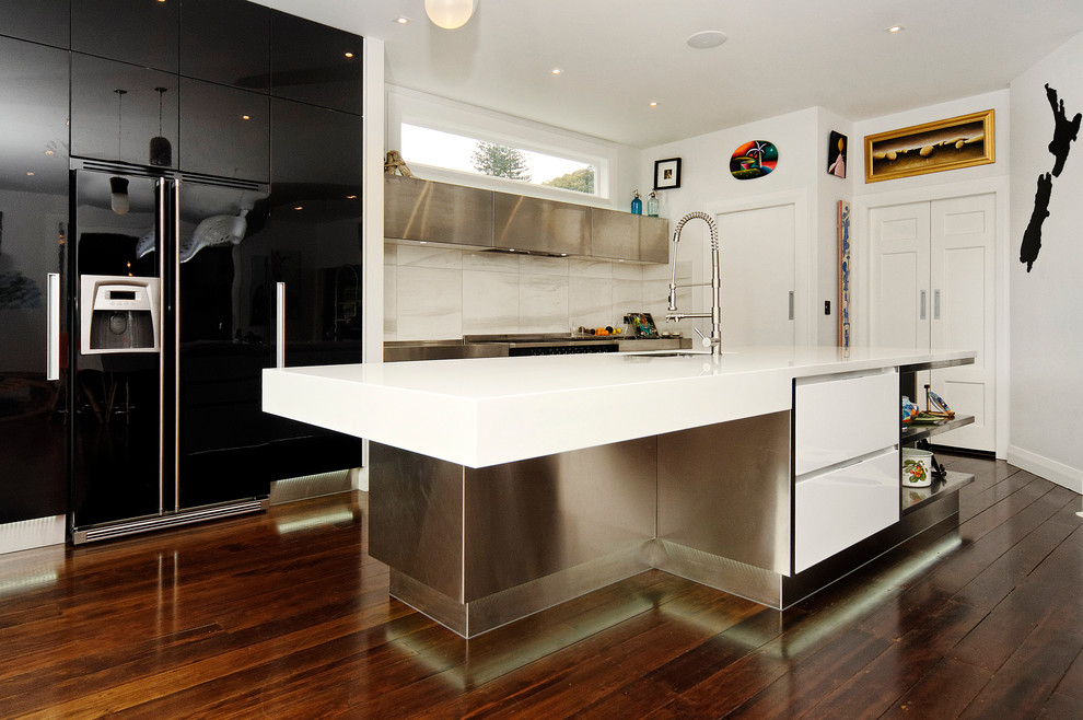 Inspiration for a mid-sized contemporary galley eat-in kitchen in Auckland with black appliances, an undermount sink, flat-panel cabinets, dark hardwood floors, with island, black cabinets, solid surface benchtops, grey splashback and stone tile splashback.