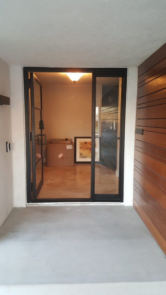 На фото: входная дверь среднего размера в стиле модернизм с коричневыми стенами, бетонным полом, одностворчатой входной дверью, черной входной дверью, серым полом и деревянными стенами