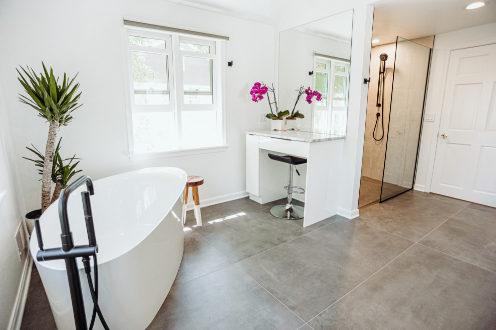 Idéer för att renovera ett stort funkis grå grått en-suite badrum, med släta luckor, vita skåp, ett fristående badkar, en kantlös dusch, en toalettstol med hel cisternkåpa, grå kakel, keramikplattor, vita väggar, klinkergolv i keramik, ett nedsänkt handfat, granitbänkskiva, grått golv och med dusch som är öppen