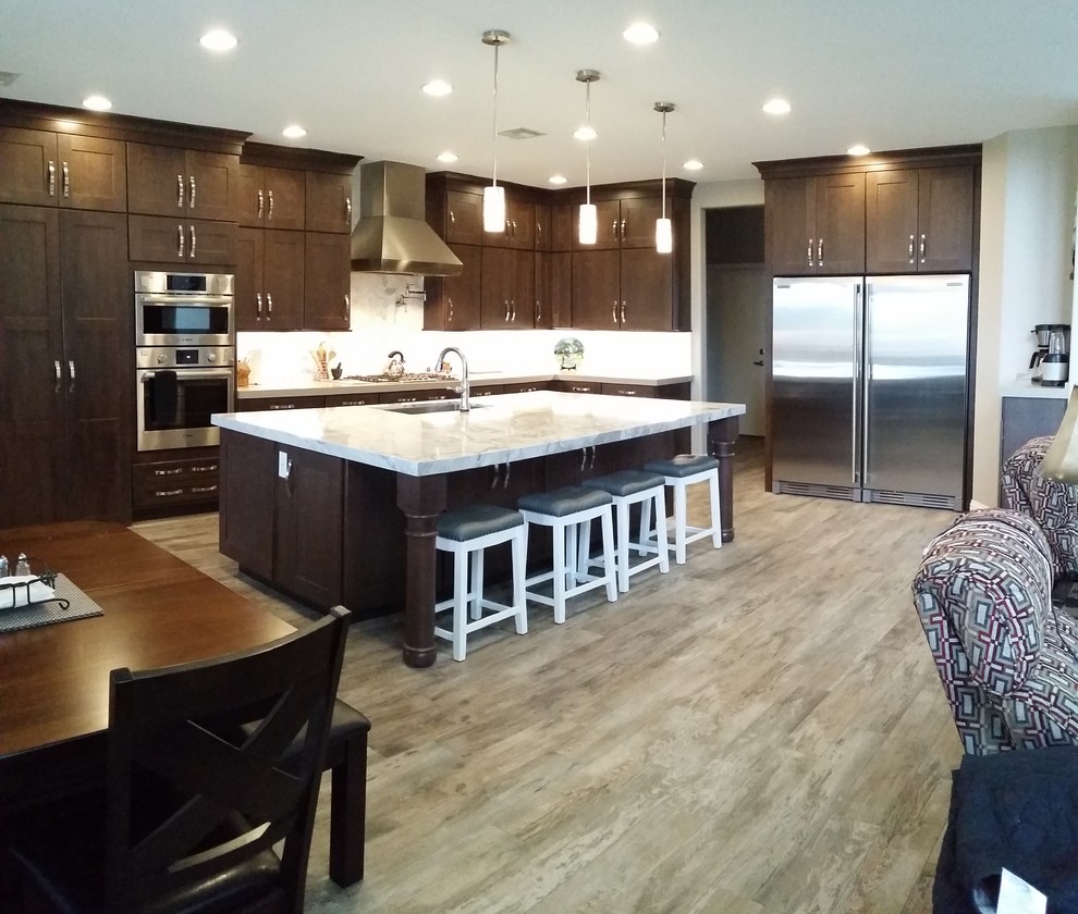 Large transitional l-shaped open plan kitchen in Las Vegas with an undermount sink, shaker cabinets, brown cabinets, quartzite benchtops, white splashback, marble splashback, stainless steel appliances, porcelain floors, with island, multi-coloured floor and grey benchtop.