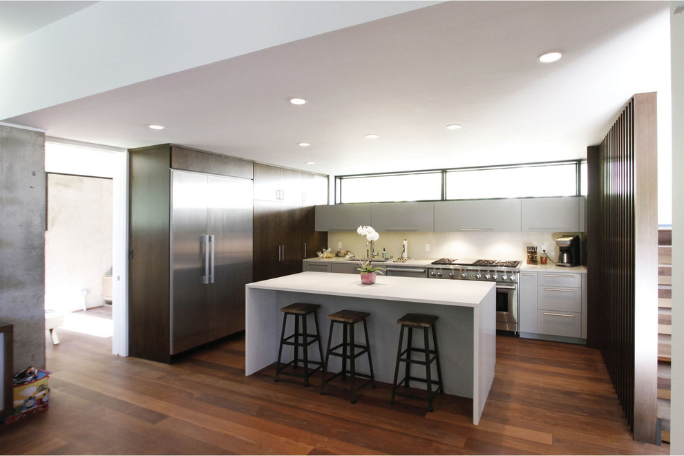 Inspiration for a mid-sized modern l-shaped medium tone wood floor and brown floor eat-in kitchen remodel in Milwaukee with an undermount sink, flat-panel cabinets, quartz countertops, white backsplash, stainless steel appliances, an island, gray cabinets and white countertops