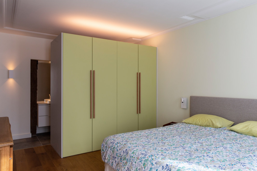 Cette image montre une grande chambre parentale design avec un mur vert, parquet clair et dressing.
