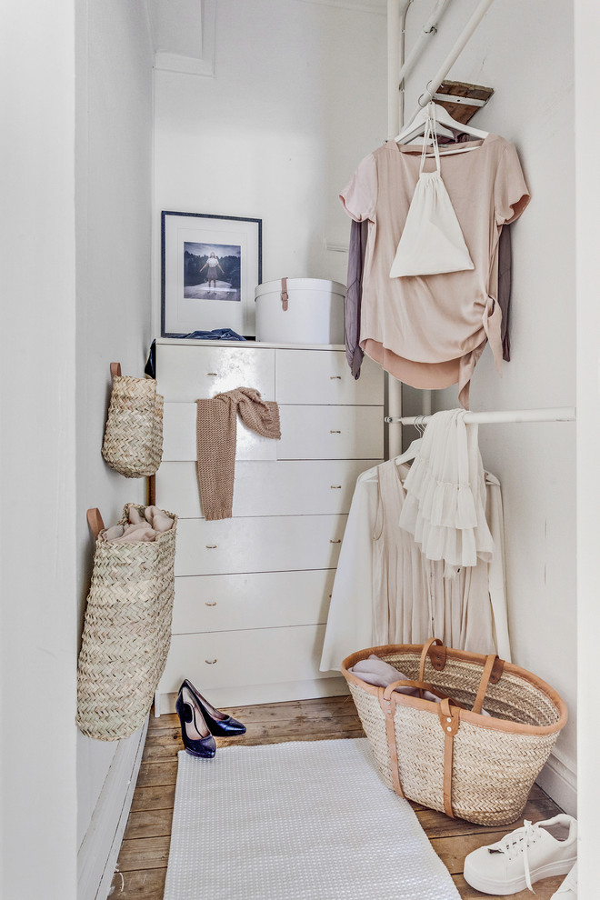 This is an example of a small scandinavian women's walk-in wardrobe in Gothenburg with open cabinets, white cabinets, light hardwood floors and brown floor.