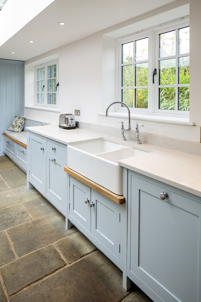 This is an example of a large country l-shaped open plan kitchen in Hertfordshire with a double-bowl sink, shaker cabinets, blue cabinets, granite benchtops, grey splashback, metal splashback, stainless steel appliances, limestone floors, with island and beige floor.