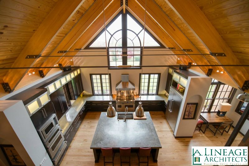 Example of a large u-shaped medium tone wood floor, brown floor and vaulted ceiling open concept kitchen design with an integrated sink, flat-panel cabinets, black cabinets, stainless steel appliances, an island and black countertops