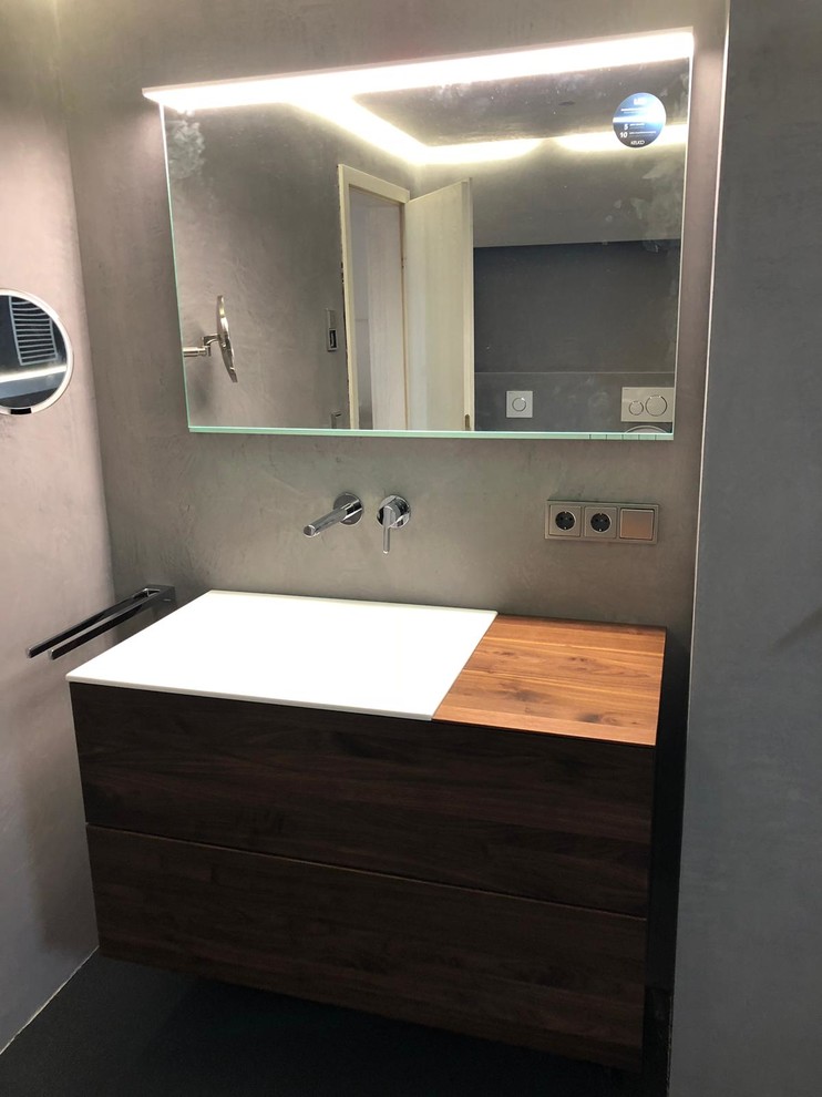 Photo of a large contemporary 3/4 bathroom in Stuttgart with flat-panel cabinets, brown cabinets, a curbless shower, a wall-mount toilet, black tile, black walls, an integrated sink, solid surface benchtops, black floor, an open shower and brown benchtops.