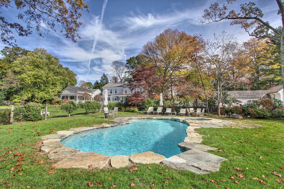 Mid-sized traditional backyard kidney-shaped pool in Other with natural stone pavers and a water feature.