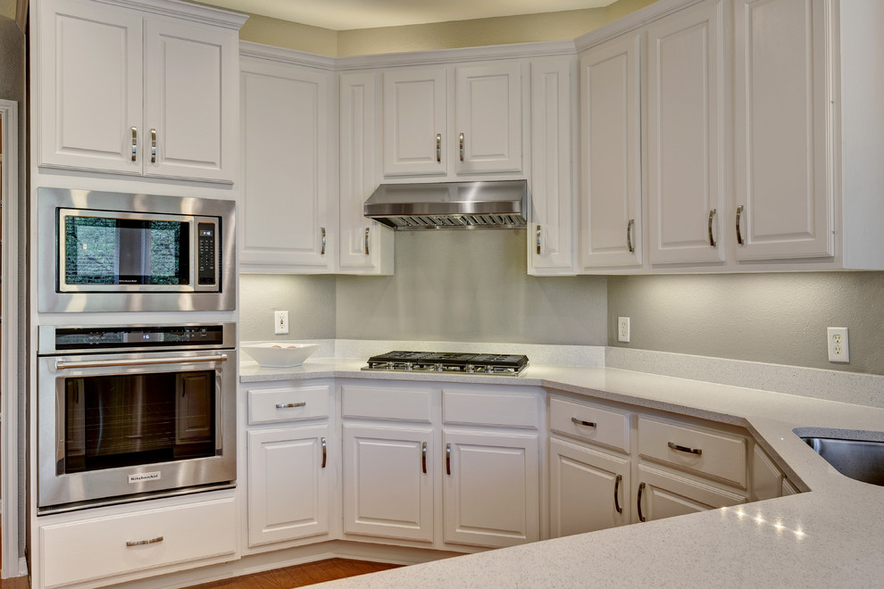 Inspiration for a mid-sized transitional u-shaped light wood floor eat-in kitchen remodel in Austin with an undermount sink, white cabinets, quartz countertops, white backsplash, stone slab backsplash, stainless steel appliances, a peninsula and raised-panel cabinets