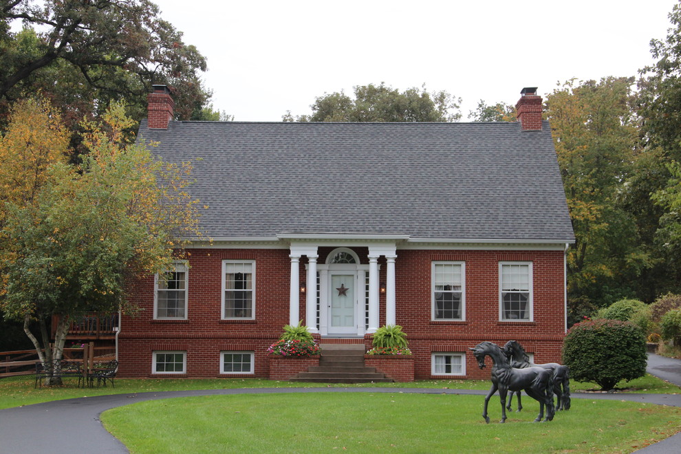 This is an example of a traditional one-storey brick red house exterior in Other with a gable roof and a shingle roof.