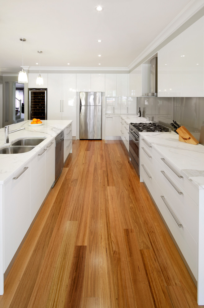 Design ideas for a mid-sized modern l-shaped kitchen in Sydney with an undermount sink, white cabinets, marble benchtops, metallic splashback, glass sheet splashback, stainless steel appliances, light hardwood floors and with island.