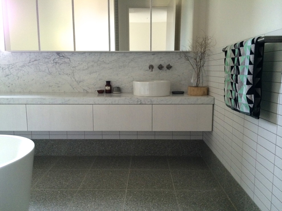 Photo of a large modern master bathroom in Melbourne with a trough sink, furniture-like cabinets, white cabinets, marble benchtops, a freestanding tub, white tile, ceramic tile and white walls.