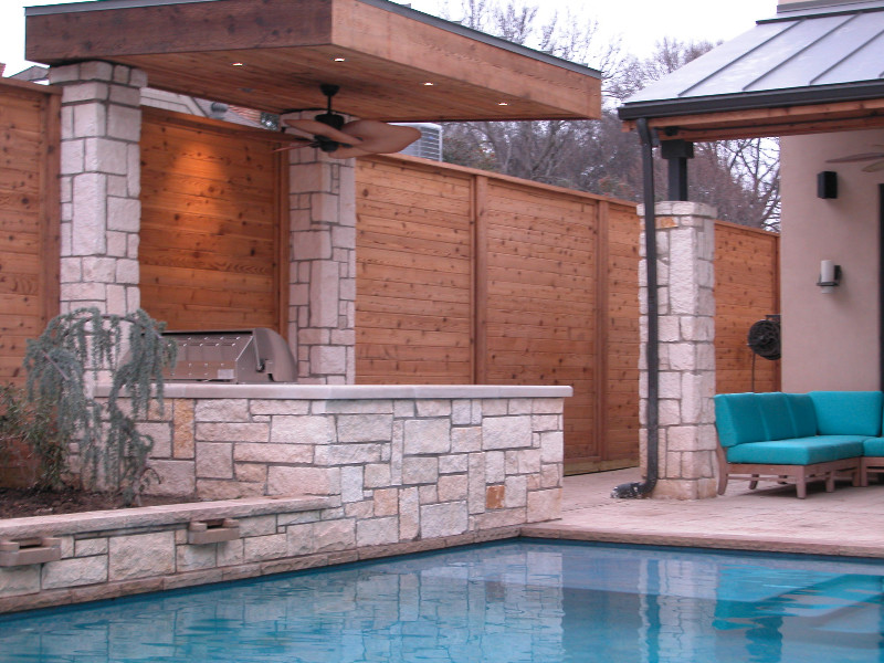 This is an example of a large transitional backyard patio in Dallas with an outdoor kitchen, natural stone pavers and a pergola.