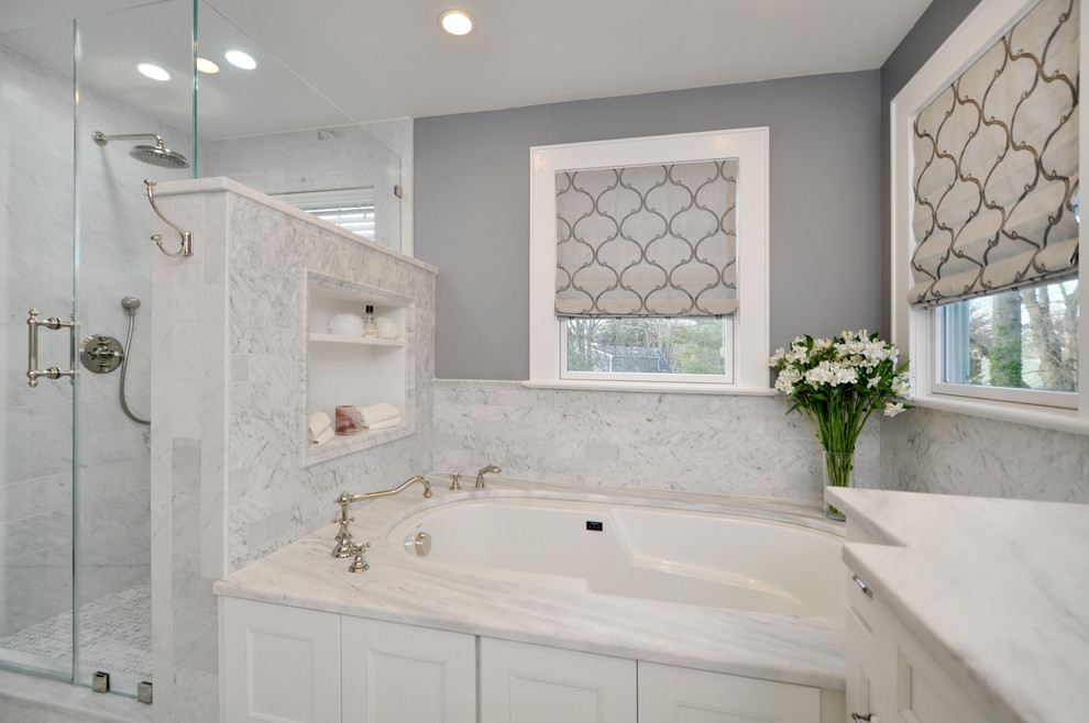 Photo of a large contemporary master bathroom in New York with recessed-panel cabinets, white cabinets, an undermount tub, a corner shower, grey walls, light hardwood floors, an undermount sink, marble benchtops, brown floor, a hinged shower door, gray tile and stone tile.