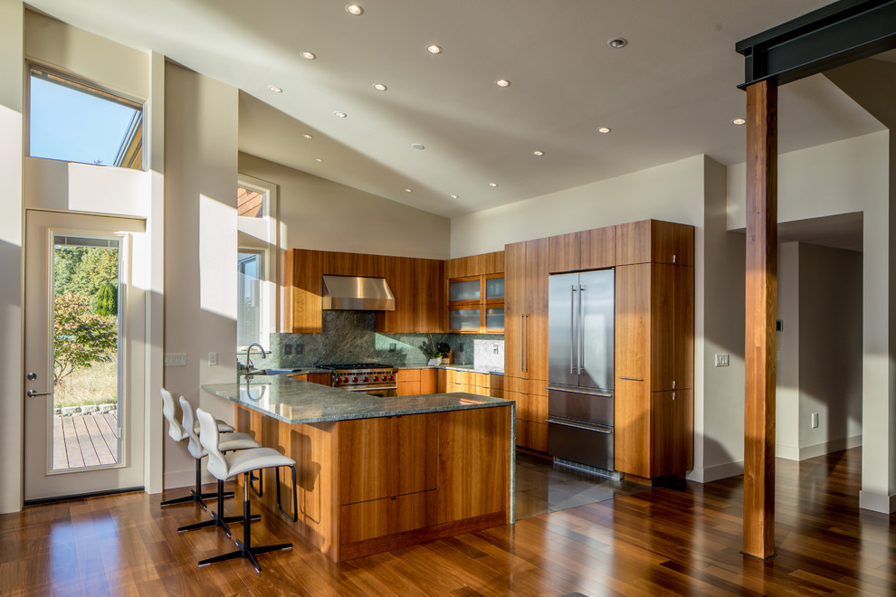 Mid-sized modern u-shaped kitchen in Seattle with a single-bowl sink, flat-panel cabinets, brown cabinets, granite benchtops, green splashback, stone slab splashback, stainless steel appliances, porcelain floors, no island, brown floor and green benchtop.