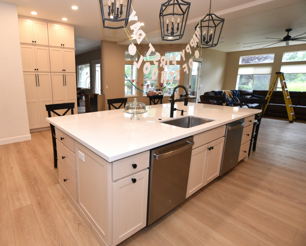 Inspiration for a large transitional l-shaped vinyl floor and beige floor kitchen remodel with an undermount sink, shaker cabinets, light wood cabinets, solid surface countertops, white backsplash, porcelain backsplash, stainless steel appliances, an island and white countertops