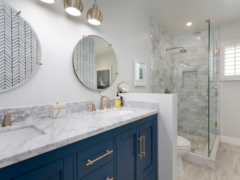 Mid-sized beach style master bathroom in Los Angeles with shaker cabinets, blue cabinets, a corner shower, a one-piece toilet, marble, grey walls, porcelain floors, an undermount sink, engineered quartz benchtops, grey floor, a hinged shower door, white benchtops, a double vanity, a built-in vanity, wallpaper and gray tile.