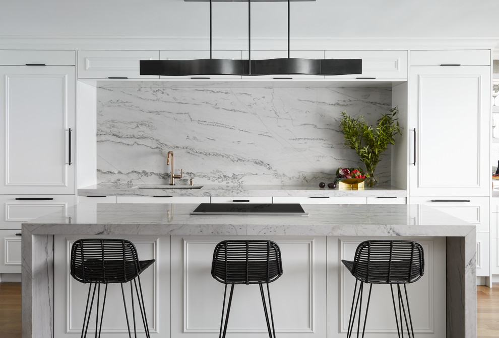 This is an example of a large contemporary galley eat-in kitchen in Chicago with an undermount sink, white cabinets, quartzite benchtops, grey splashback, stone slab splashback, panelled appliances, medium hardwood floors, with island, grey benchtop, recessed-panel cabinets and brown floor.