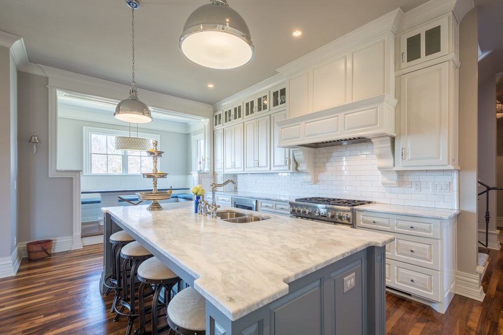 This is an example of a large transitional l-shaped eat-in kitchen in Louisville with a double-bowl sink, raised-panel cabinets, white cabinets, marble benchtops, white splashback, subway tile splashback, stainless steel appliances, dark hardwood floors and with island.