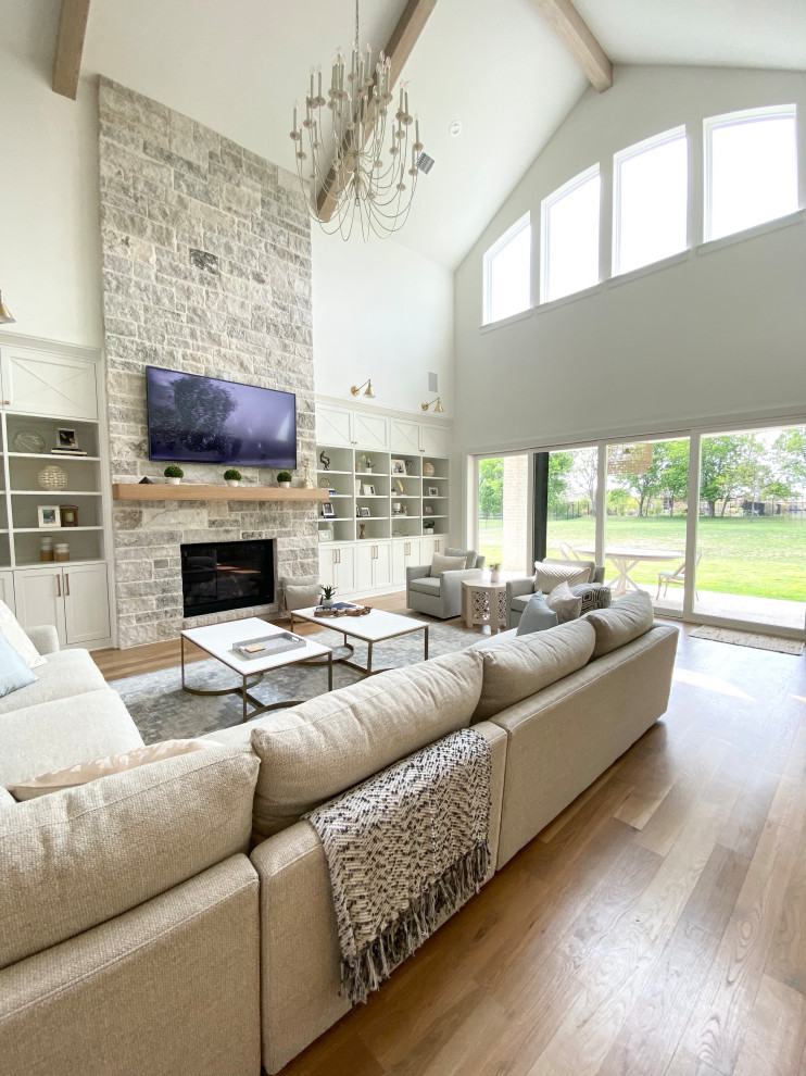 This is an example of an expansive scandinavian open plan games room in Dallas with white walls, light hardwood flooring, all types of fireplace, a stone fireplace surround, a wall mounted tv, beige floors and exposed beams.