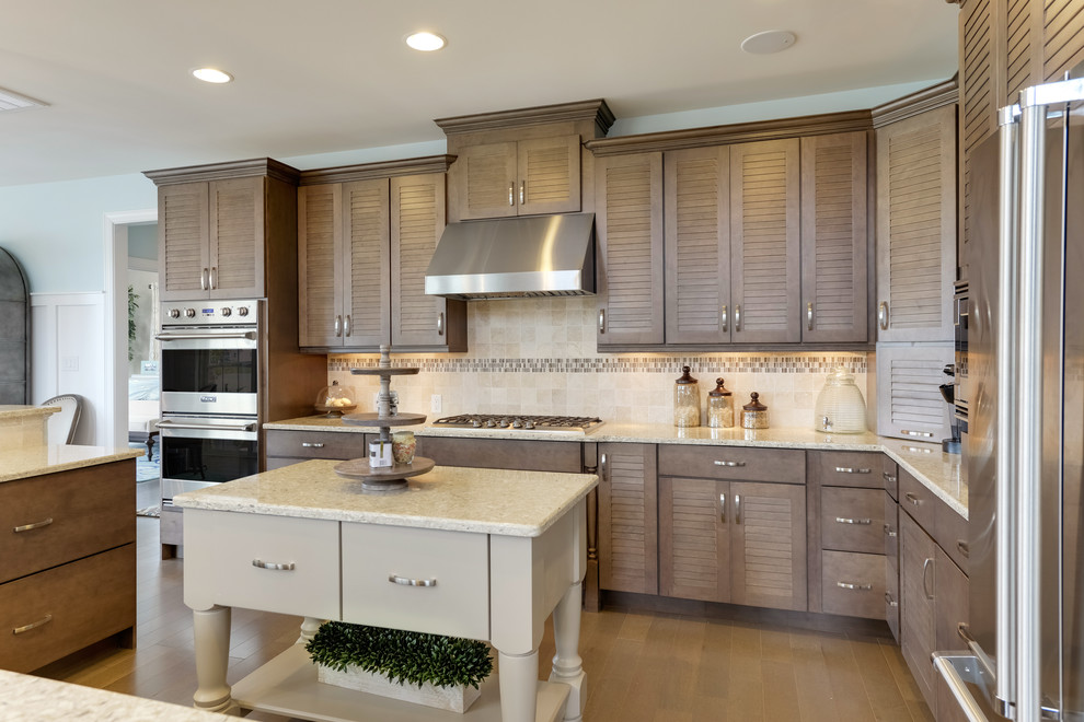 Photo of a large beach style eat-in kitchen in Other with louvered cabinets, brown cabinets, quartz benchtops, beige splashback, mosaic tile splashback, stainless steel appliances, medium hardwood floors, multiple islands and brown floor.