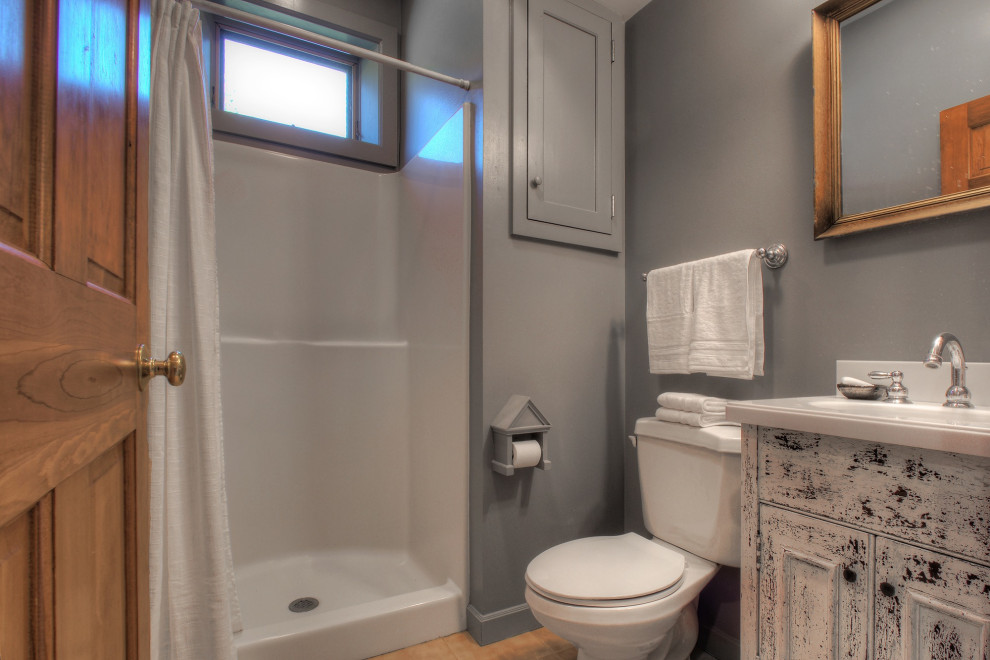 Photo of a small country 3/4 bathroom in New York with raised-panel cabinets, distressed cabinets, an alcove shower, a two-piece toilet, grey walls, porcelain floors, an integrated sink, laminate benchtops, orange floor, a shower curtain, white benchtops, a single vanity and a built-in vanity.