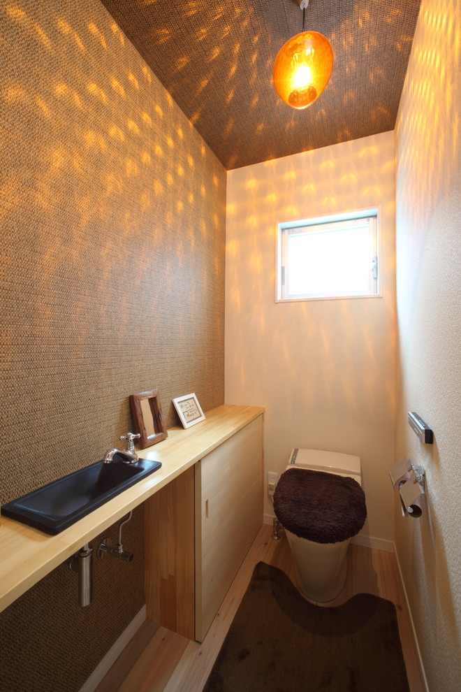 Asian powder room in Other with flat-panel cabinets, light wood cabinets, brown walls, light hardwood floors, a drop-in sink, wood benchtops, beige floor and beige benchtops.