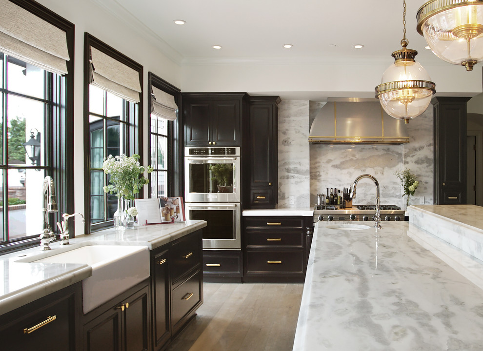 Design ideas for a traditional u-shaped kitchen in Phoenix with a farmhouse sink, recessed-panel cabinets, black cabinets, white splashback, stone slab splashback, stainless steel appliances, light hardwood floors, with island, beige floor, white benchtop and marble benchtops.