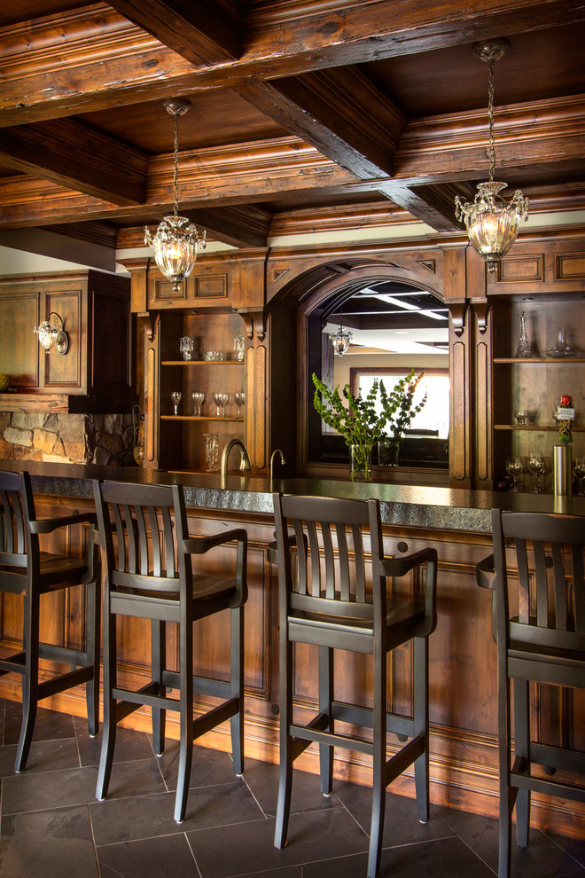 This is an example of a large country seated home bar in Other with recessed-panel cabinets, granite benchtops, medium wood cabinets and grey floor.
