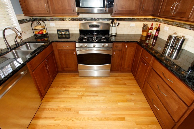 Enclosed kitchen - mid-sized transitional u-shaped light wood floor enclosed kitchen idea in Chicago with an undermount sink, shaker cabinets, medium tone wood cabinets, granite countertops, beige backsplash, stone tile backsplash, stainless steel appliances and no island