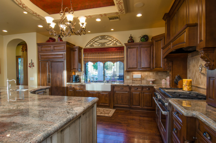 Inspiration for a huge transitional u-shaped dark wood floor kitchen remodel in Phoenix with a farmhouse sink, dark wood cabinets, granite countertops, beige backsplash, stone tile backsplash, stainless steel appliances and an island