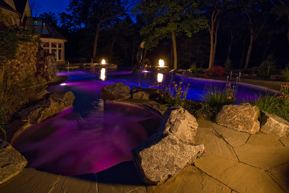 Photo of an expansive mediterranean backyard custom-shaped infinity pool in Chicago with natural stone pavers and a hot tub.