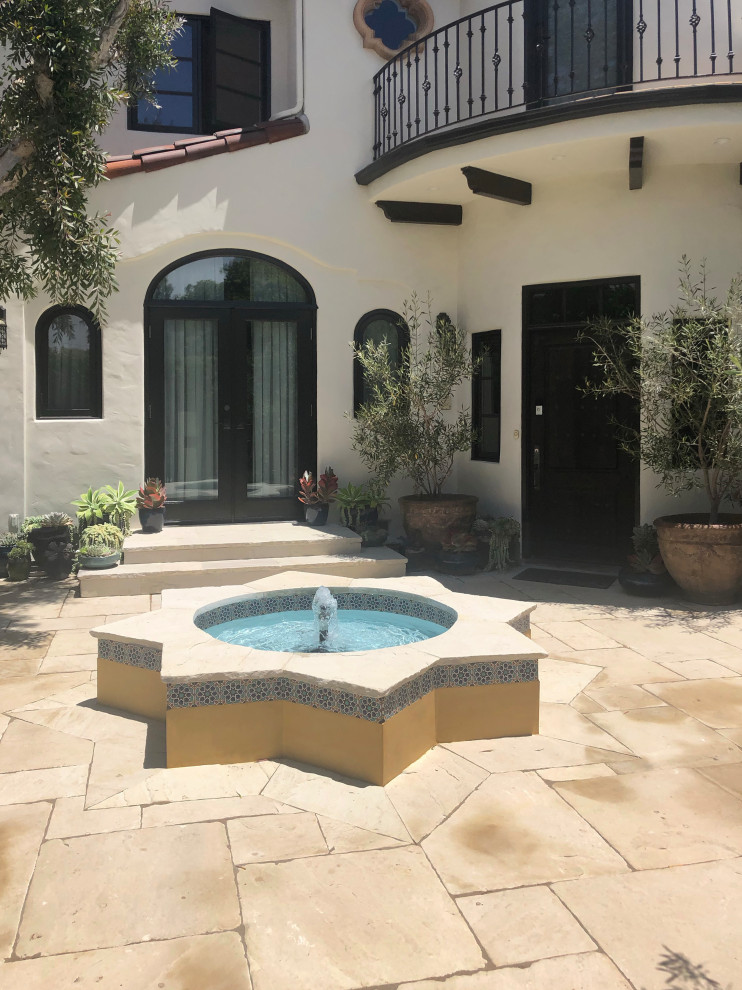 Diseño de jardín de secano mediterráneo de tamaño medio en primavera en patio con fuente, exposición parcial al sol, adoquines de piedra natural y con piedra