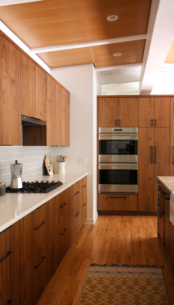 This is an example of a mid-sized midcentury single-wall eat-in kitchen in Detroit with a drop-in sink, flat-panel cabinets, medium wood cabinets, quartzite benchtops, grey splashback, ceramic splashback, stainless steel appliances, medium hardwood floors, with island, orange floor and beige benchtop.