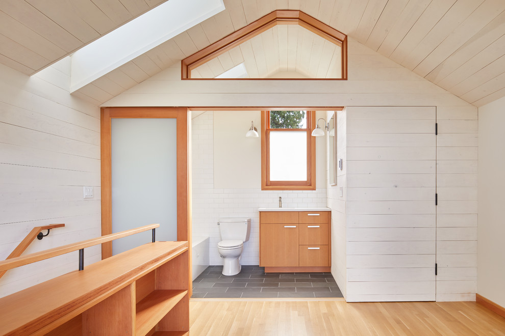 This is an example of a small contemporary master bathroom in Seattle with flat-panel cabinets, medium wood cabinets, an alcove tub, a shower/bathtub combo, a two-piece toilet, white tile, subway tile, white walls, slate floors, an undermount sink, engineered quartz benchtops, grey floor, a shower curtain and white benchtops.
