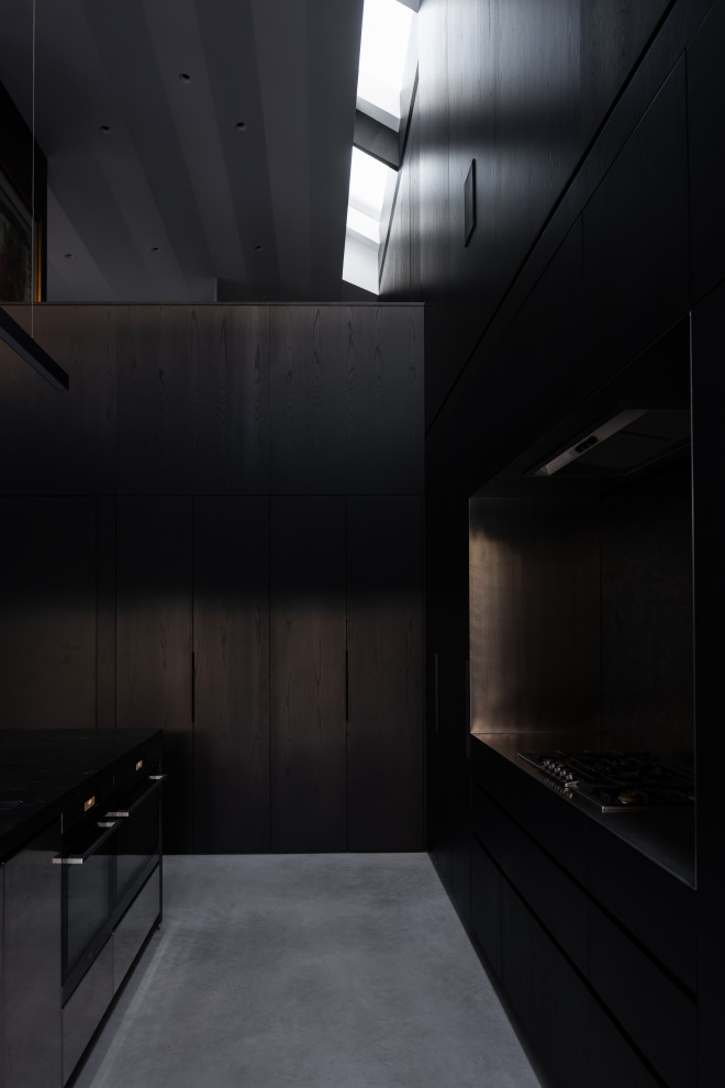 Photo of an expansive contemporary galley eat-in kitchen in Sydney with an undermount sink, black cabinets, quartz benchtops, black splashback, stone slab splashback, black appliances, concrete floors, with island, grey floor and black benchtop.