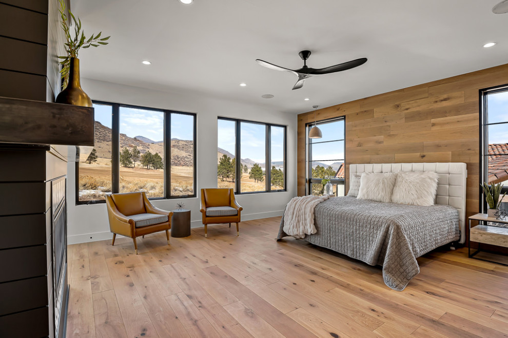 Large modern master bedroom in Denver with white walls, light hardwood flooring, a standard fireplace, a timber clad chimney breast and brown floors.