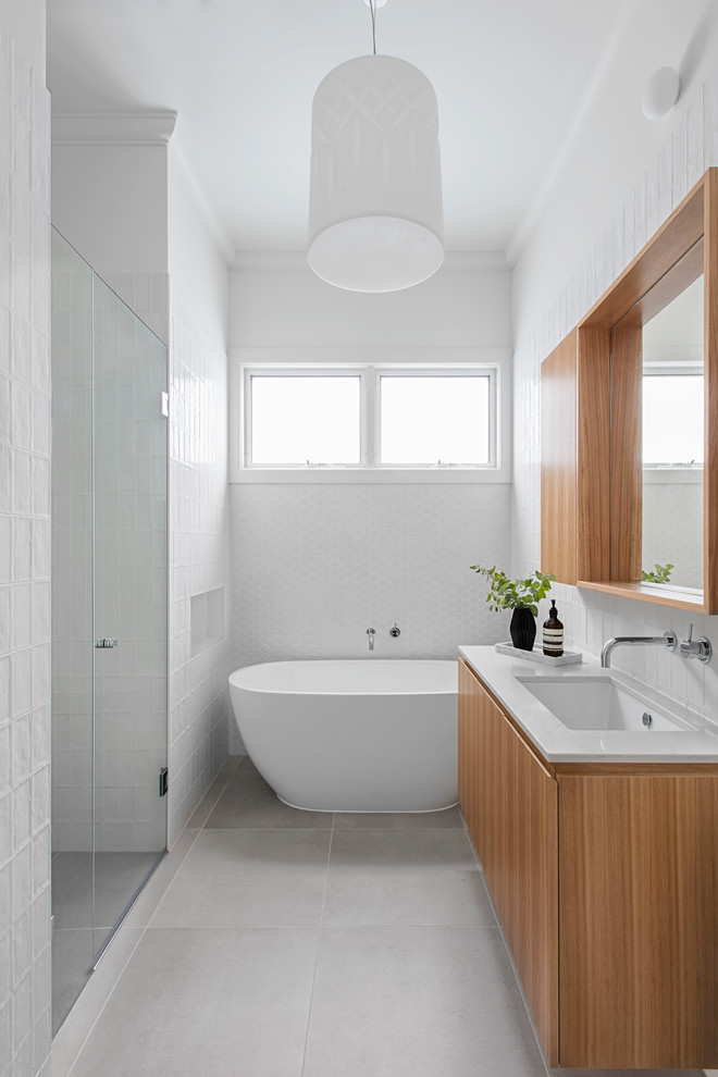 Mid-sized contemporary bathroom in Melbourne with medium wood cabinets, a freestanding tub, white tile, porcelain floors, an undermount sink, engineered quartz benchtops, grey floor, a hinged shower door, white benchtops and white walls.
