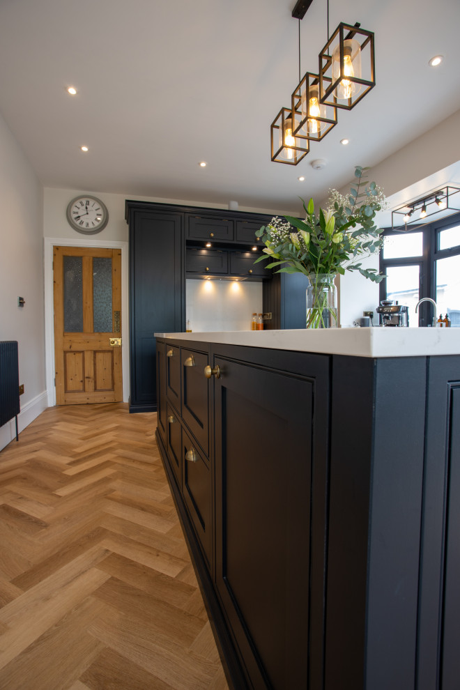 Design ideas for a mid-sized traditional eat-in kitchen in Essex with shaker cabinets, black cabinets, quartzite benchtops, white splashback, medium hardwood floors, with island, brown floor and white benchtop.