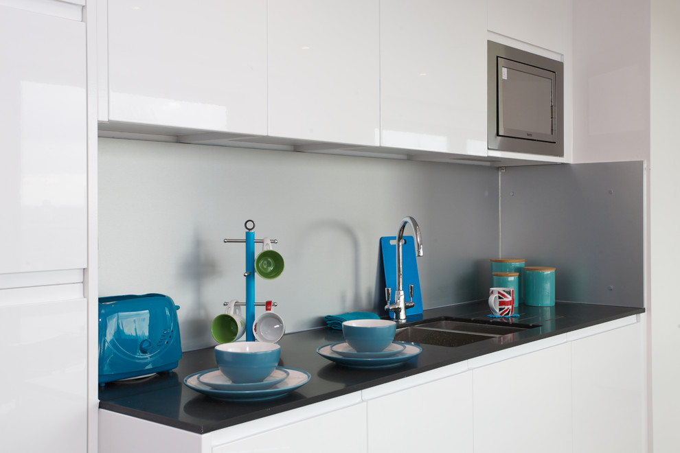 Small contemporary single-wall eat-in kitchen in London with an undermount sink, flat-panel cabinets, white cabinets, quartz benchtops, metallic splashback, black appliances and no island.