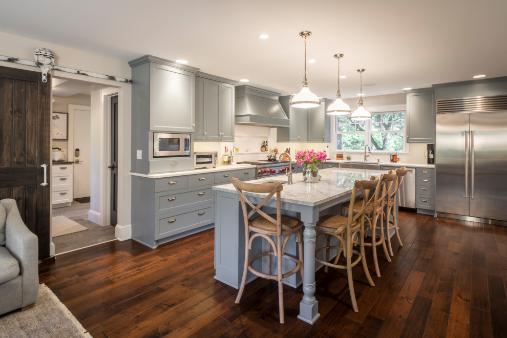 Design ideas for a large transitional l-shaped kitchen in Minneapolis with a farmhouse sink, shaker cabinets, grey cabinets, white splashback, stainless steel appliances, medium hardwood floors, with island, brown floor and grey benchtop.
