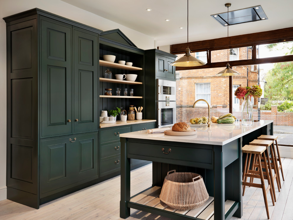Traditional galley kitchen in Oxfordshire with recessed-panel cabinets, green cabinets, stainless steel appliances, light hardwood floors and with island.