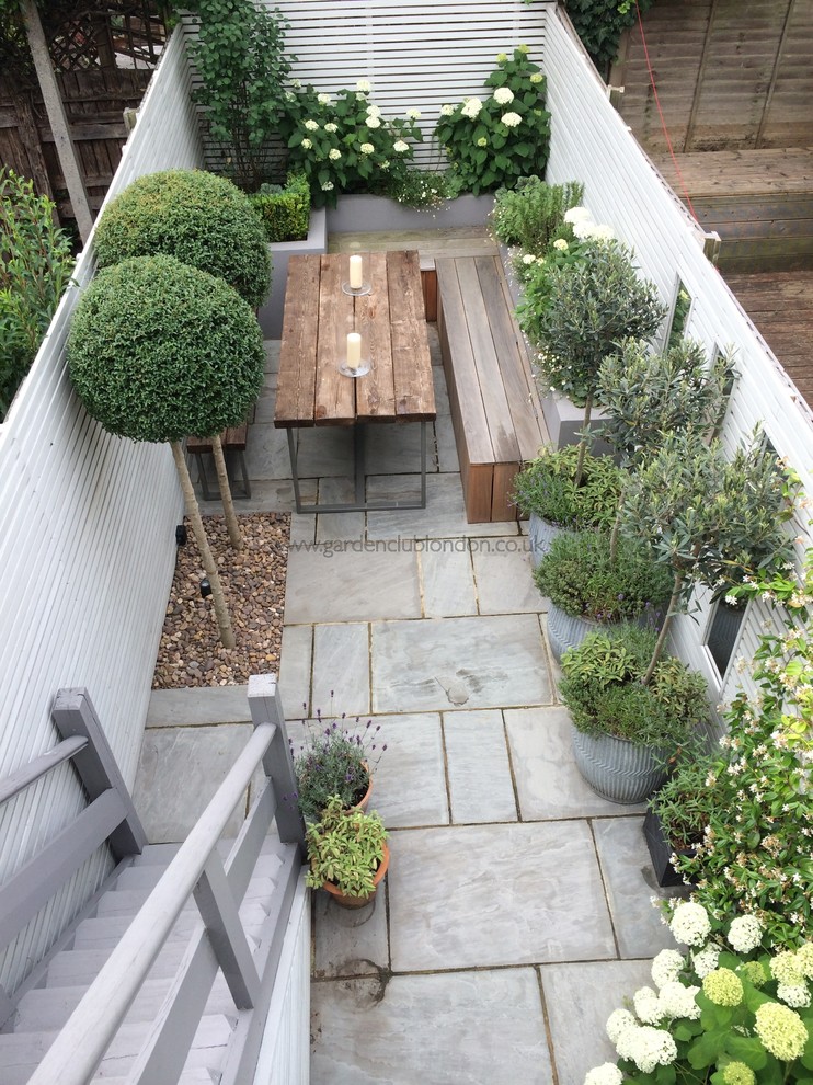 Design ideas for a small modern backyard shaded garden for summer in London with a container garden and natural stone pavers.