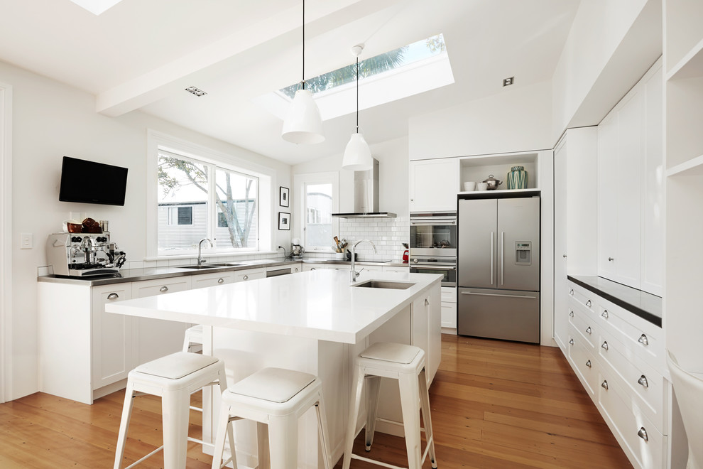 Design ideas for a transitional u-shaped kitchen in Auckland with a double-bowl sink, recessed-panel cabinets, white cabinets, white splashback, subway tile splashback and stainless steel appliances.