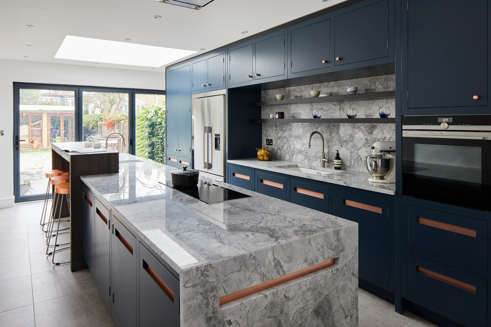 This is an example of a large contemporary single-wall kitchen in London with a drop-in sink, flat-panel cabinets, blue cabinets, granite benchtops, grey splashback, marble splashback, stainless steel appliances, ceramic floors, with island, grey floor and grey benchtop.