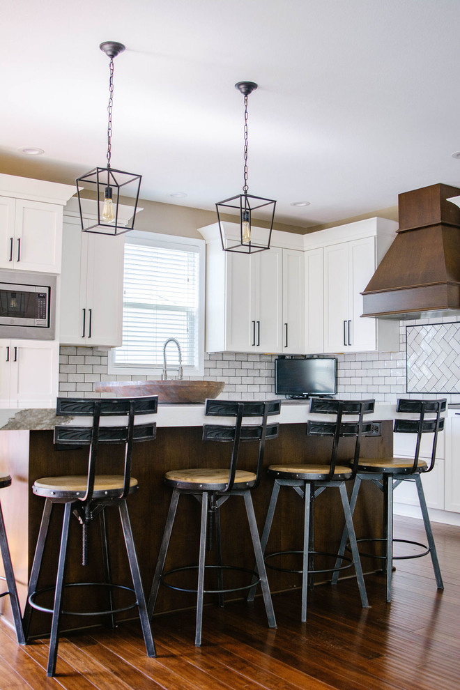 Inspiration for a mid-sized transitional l-shaped medium tone wood floor and brown floor eat-in kitchen remodel in Omaha with a farmhouse sink, shaker cabinets, white cabinets, quartzite countertops, white backsplash, subway tile backsplash, stainless steel appliances, an island and white countertops
