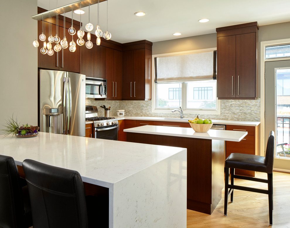 Photo of a small eclectic u-shaped eat-in kitchen in Chicago with an undermount sink, flat-panel cabinets, brown cabinets, quartz benchtops, white splashback, glass tile splashback, stainless steel appliances, light hardwood floors and with island.